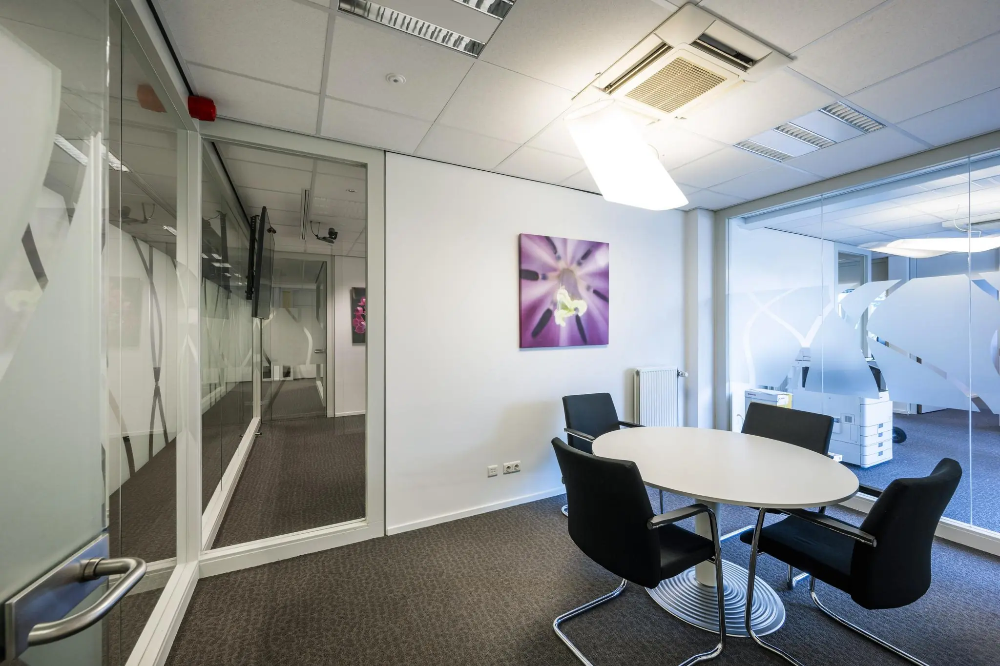 Moderne vergaderruimte aan de Jan Tooropstraat met glazen wanden, een ronde tafel en vier zwarte stoelen.